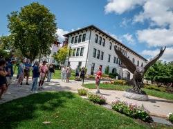 A man standing in front of a giant red hawk statue speaks to a group of people about Montclair State University.